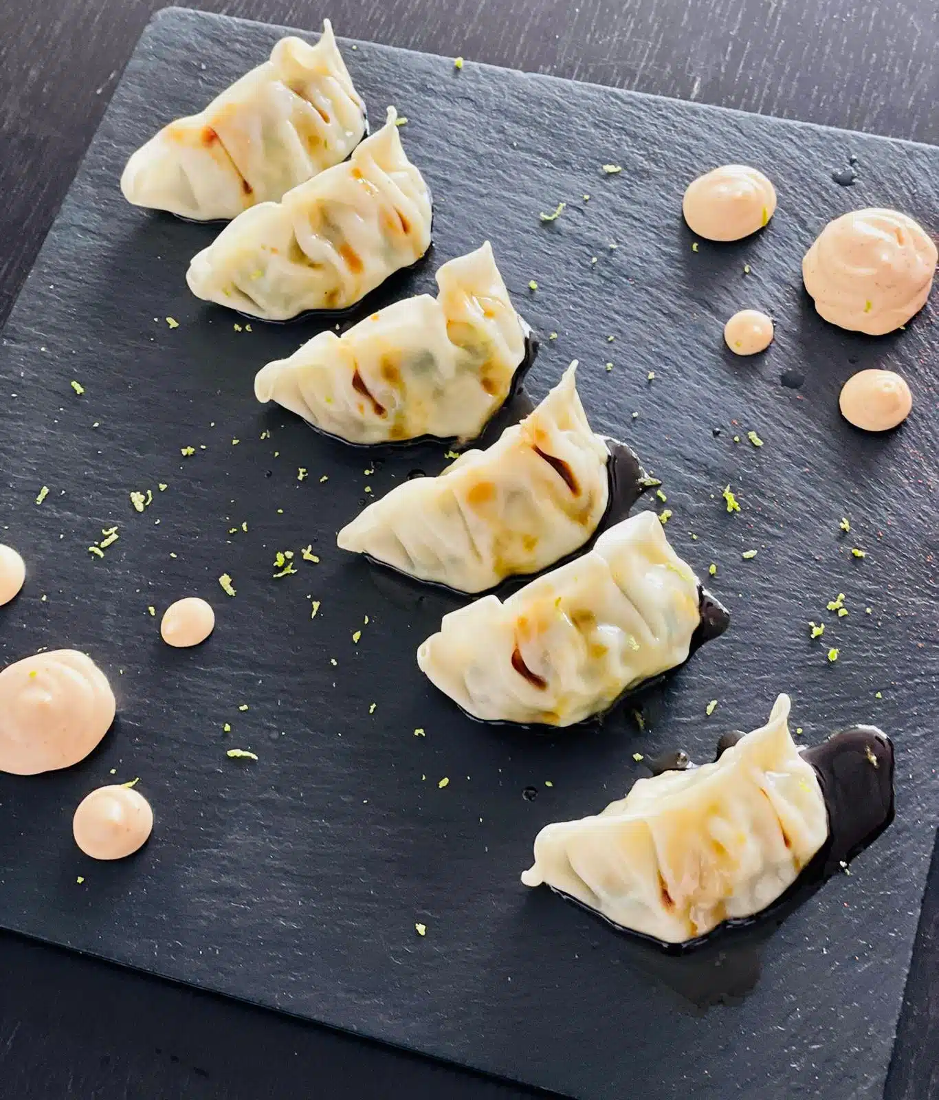 Gyozas presentadas sobre pizarra con salsas y polvo de hierbas en catering creativo